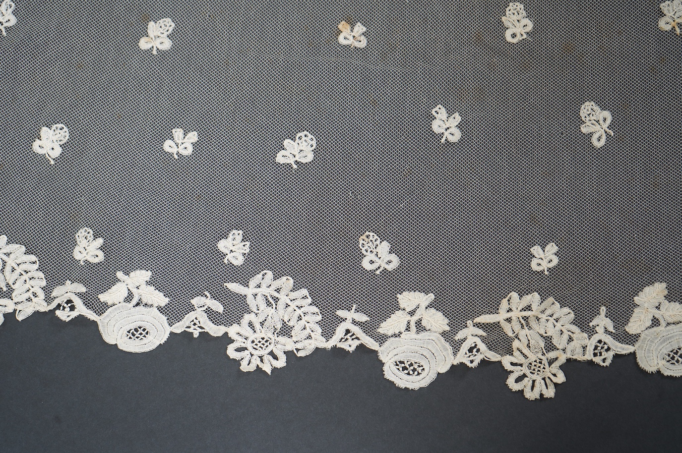 An Edwardian Brussels bobbin lace on net wedding veil, with all over bobbin lace appliqué spot motifs, within an ornate bobbin lace border, approximately 175cm x 168cm. Condition - there are various rust stains and holes